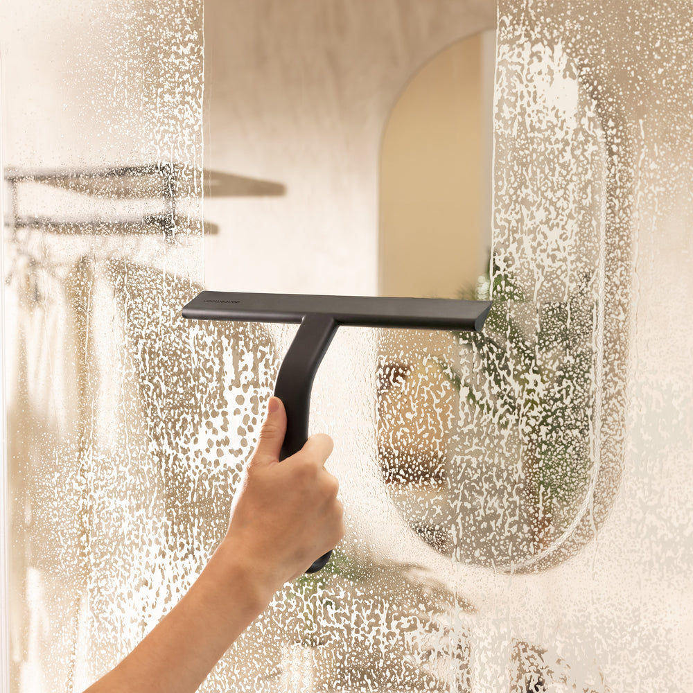 Black JustHang shower squeegee wiping soap suds from shower glass
