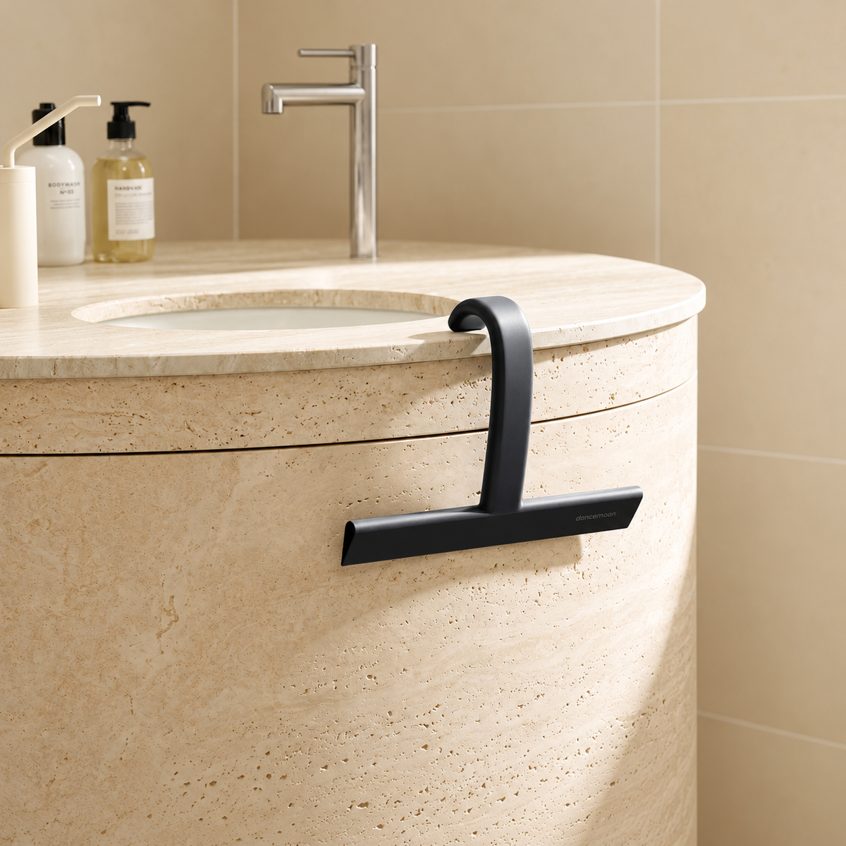 Black dancemoon JustHang shower squeegee hanging on a beige stone bathroom counter.