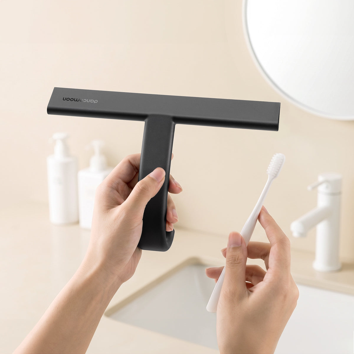 Black dancemoon JustHang Compact shower squeegee held next to a white toothbrush above a bathroom sink for size comparison